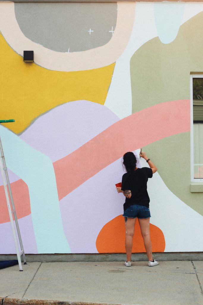 Image of Natasha Runions painting her mural on the side of the SuzyQ Doughnuts building at 2015 Robertson Road in Bells Corners.